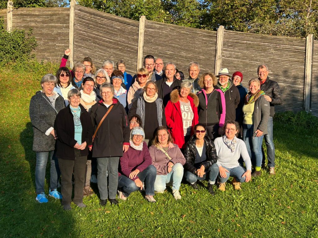 Bei sonnigem Wetter posieren viele Kolleginnen und Kollegen nach dem Minigolf-Mitarbeiterevent vor einer Holzbegrenzung auf der Wiese.