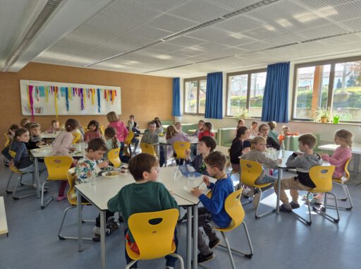 In der hellen neuen Mensa an der Leo-von-Welden-Schule Bad Feilnbach sitzen Kinder an Tischen und essen gemeinsam das Mittagessen in ruhiger Atmosphäre.
